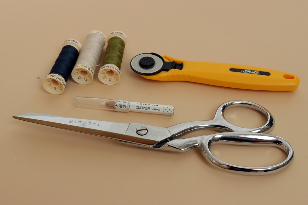 a flat lay of sewing tools, including scissors, chalk, thread, and a rotary cutter