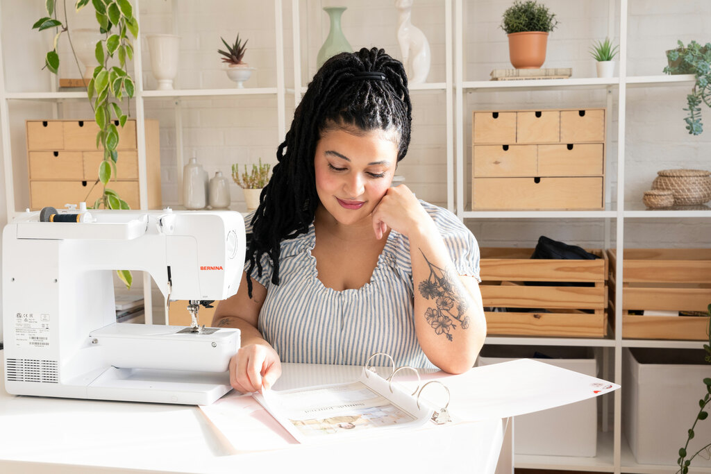 A woman sits by a sewing machine and contemplates her plans